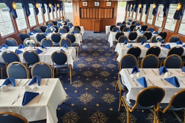 Interior of a dining cruise ship with tables set for an event, decorated with blue chairs and white tablecloths.
