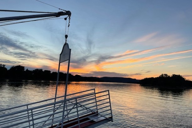 Sunset view with a dock structure over a calm lake with silhouetted trees in the background.