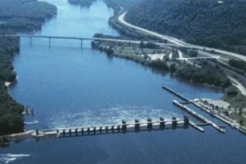 Aerial view of a river with a bridge, dam, and surrounding forested area.